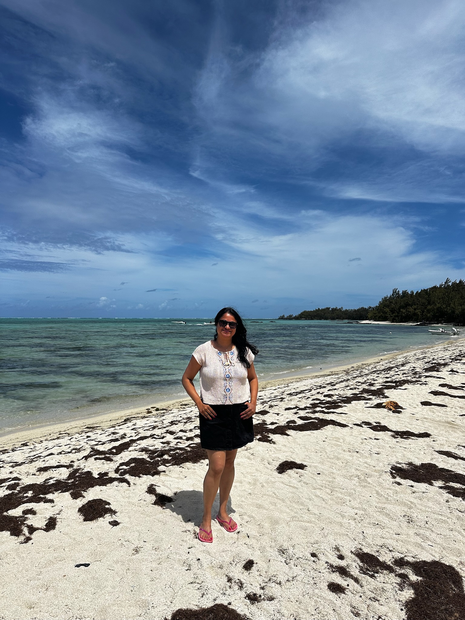 A woman standing on a sandy beach with a vibrant blue sky and gentle waves in the background.