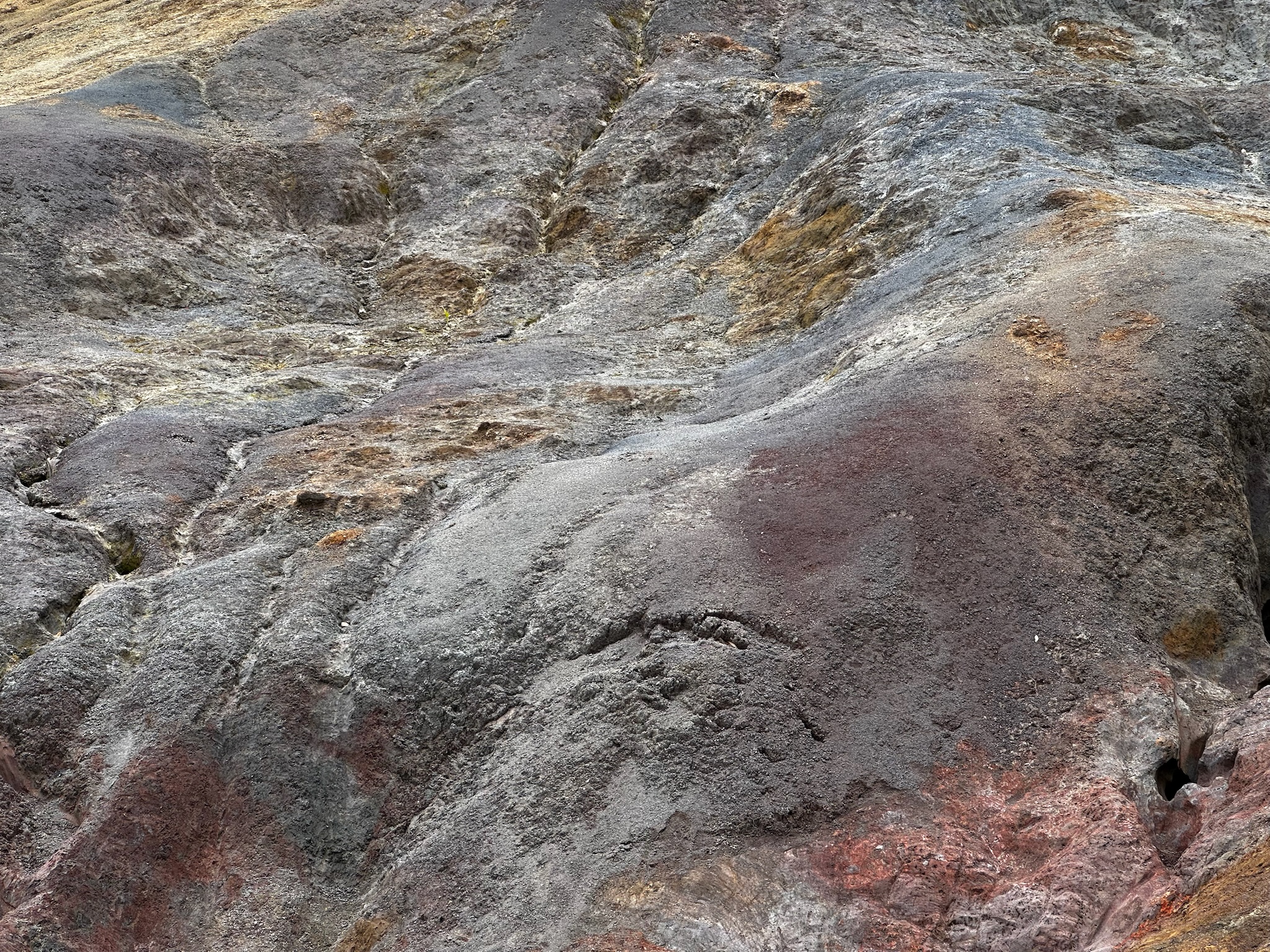 Close-up view of colorful rocky terrain with shades of gray, red, and yellow, showcasing natural textures and patterns.