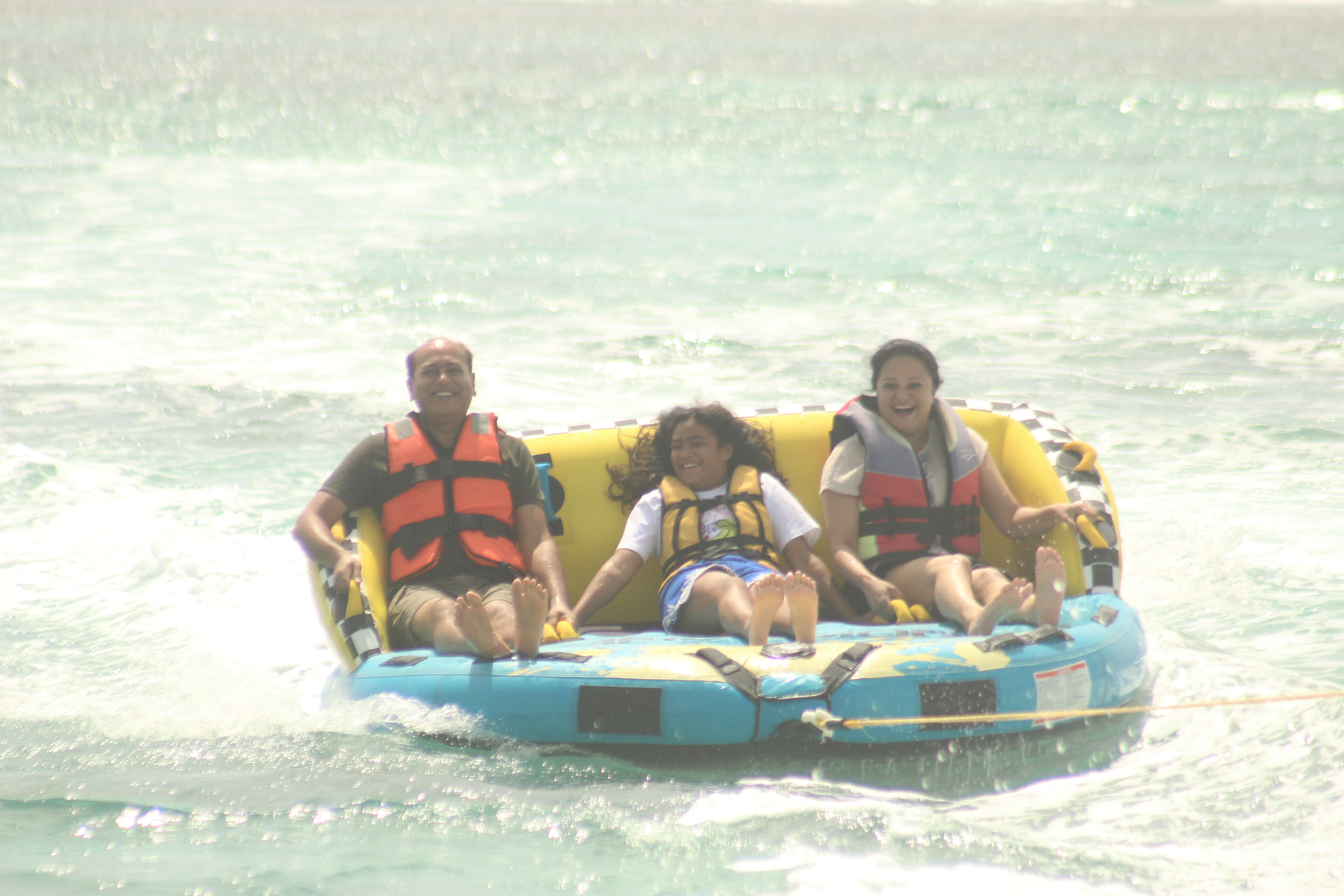 Three people enjoying a thrilling ride on a banana boat in the ocean, wearing life jackets and smiling as they skim across the water.